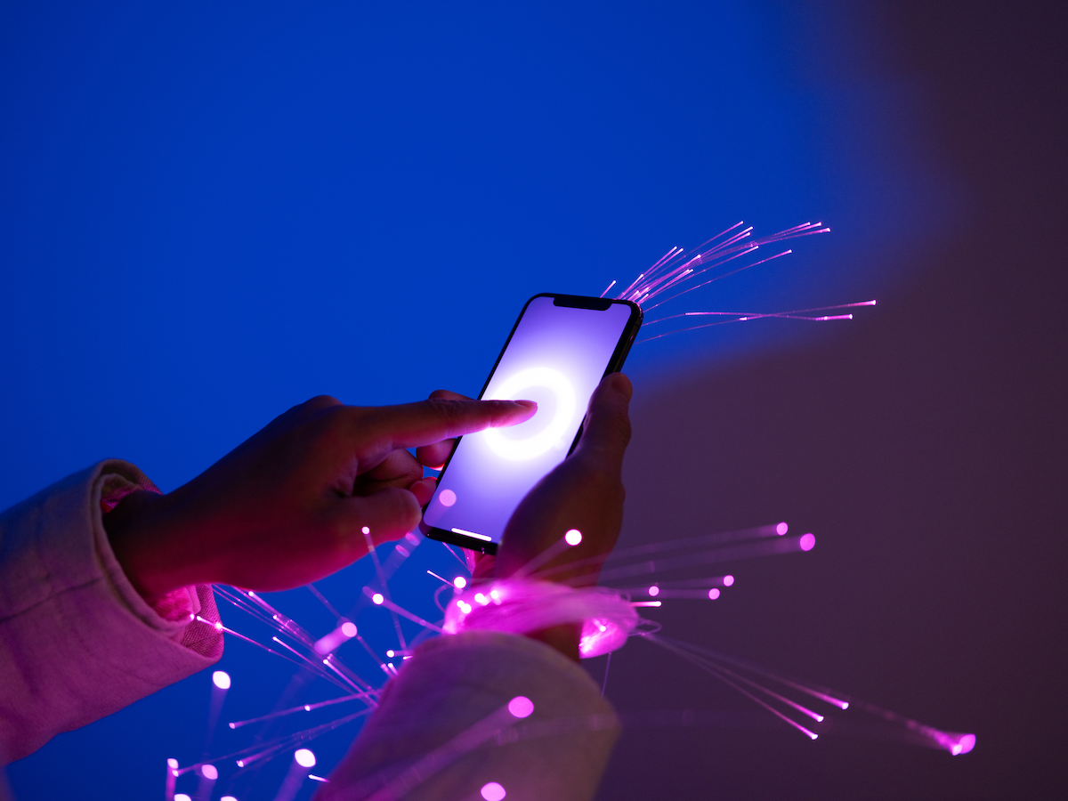 Close-up of holding smartphone, with fiber optics and cybersecurity background.